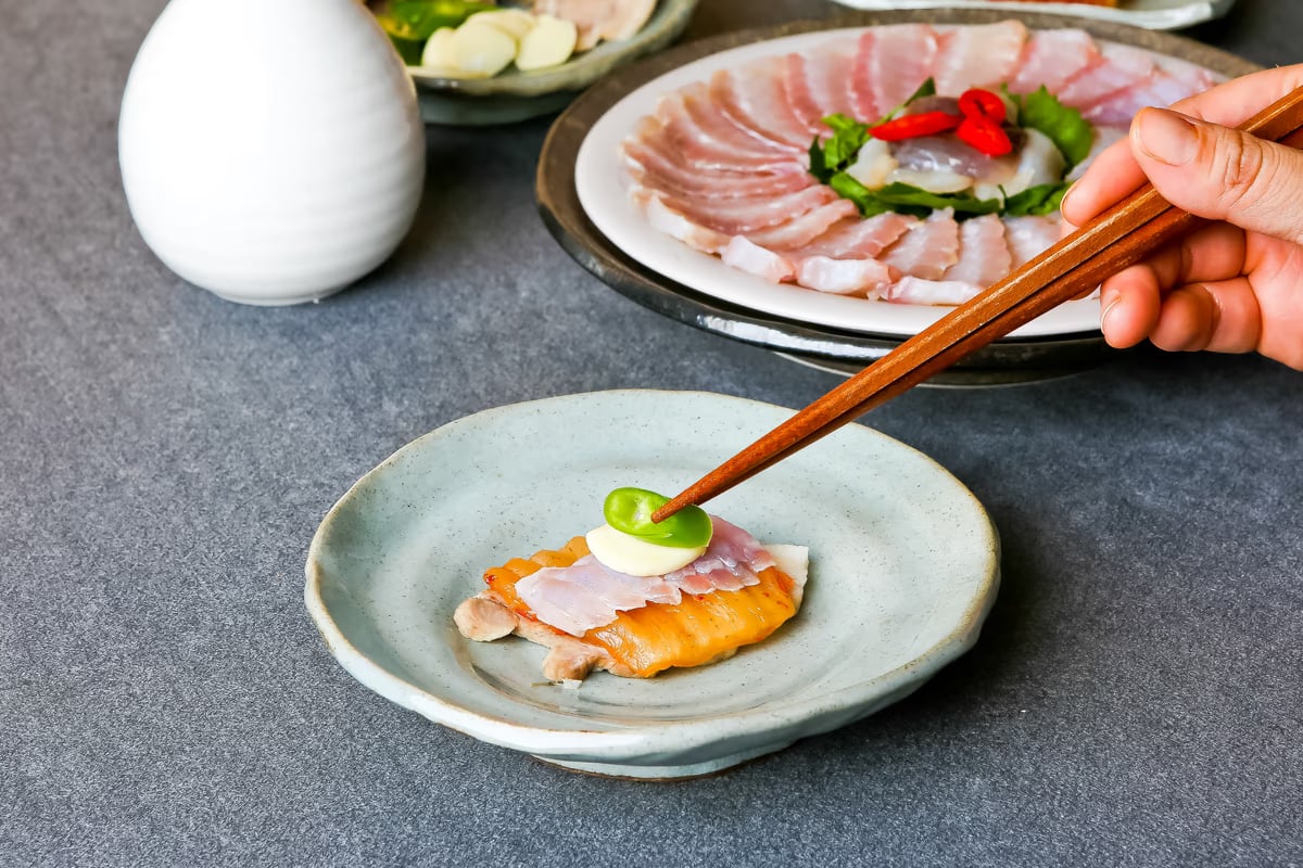 홍어삼합 한 점 올리기 — 수육 위에 홍어와 묵은지를 젓가락으로 조립하는 장면