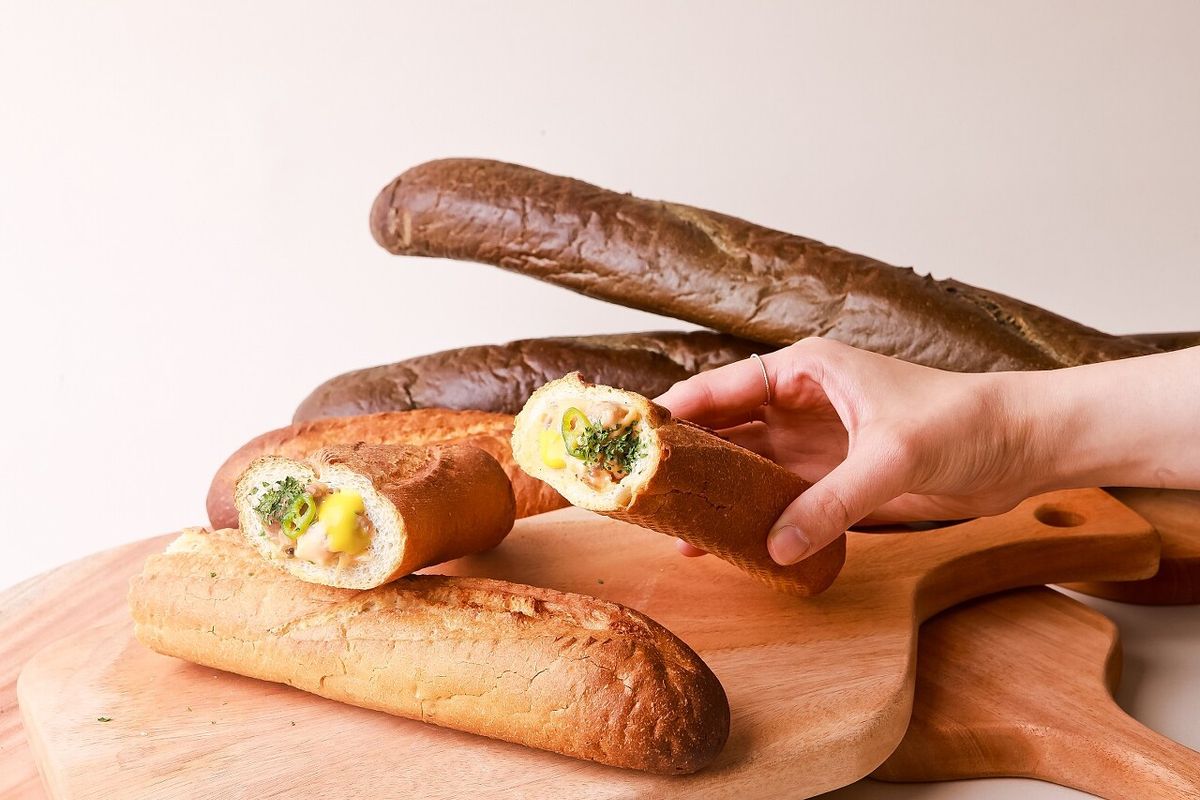 한 손으로 단면을 보여주고, 아래에 통째 바게뜨가 놓인 구도