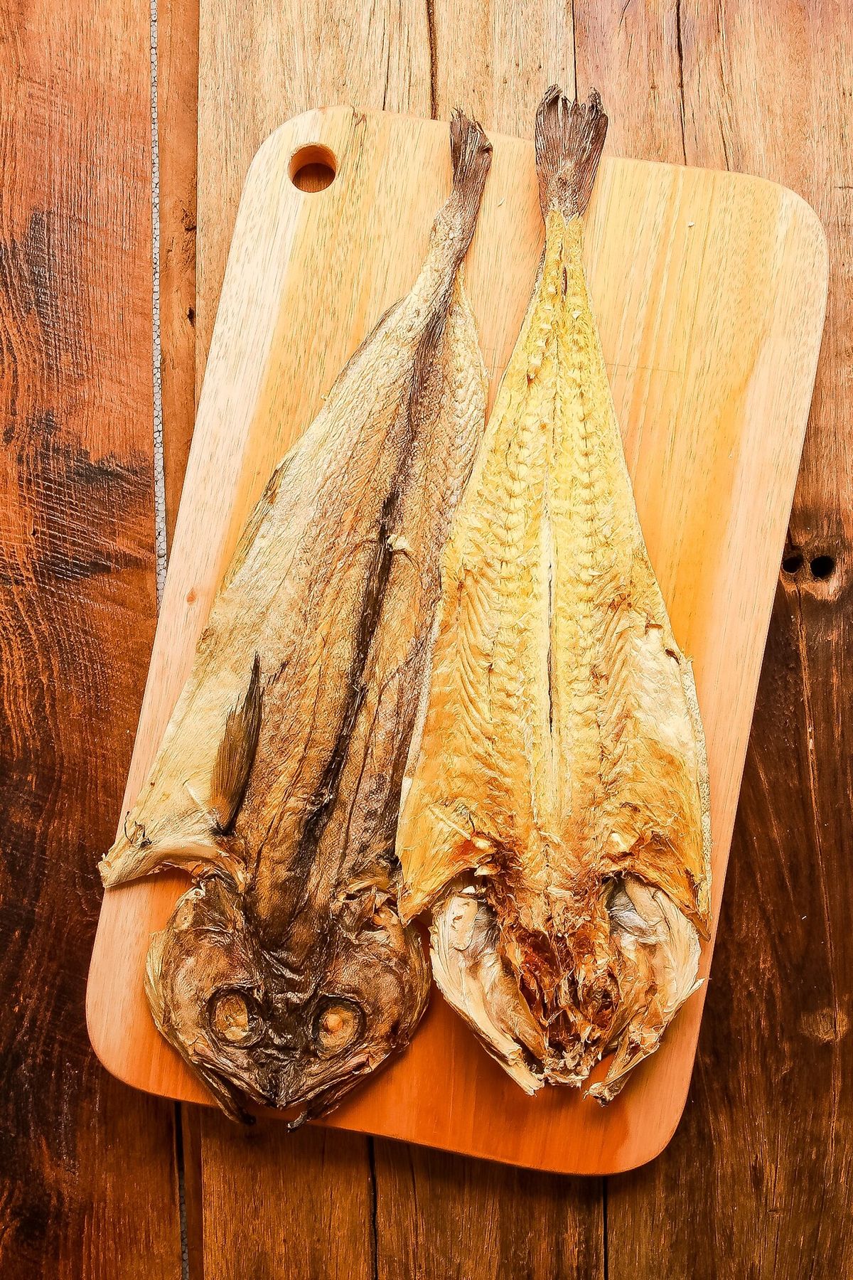 통황태 두 마리 원목 테이블 배경, 따뜻한 나무 색감과 황금빛 황태가 어우러진 컷