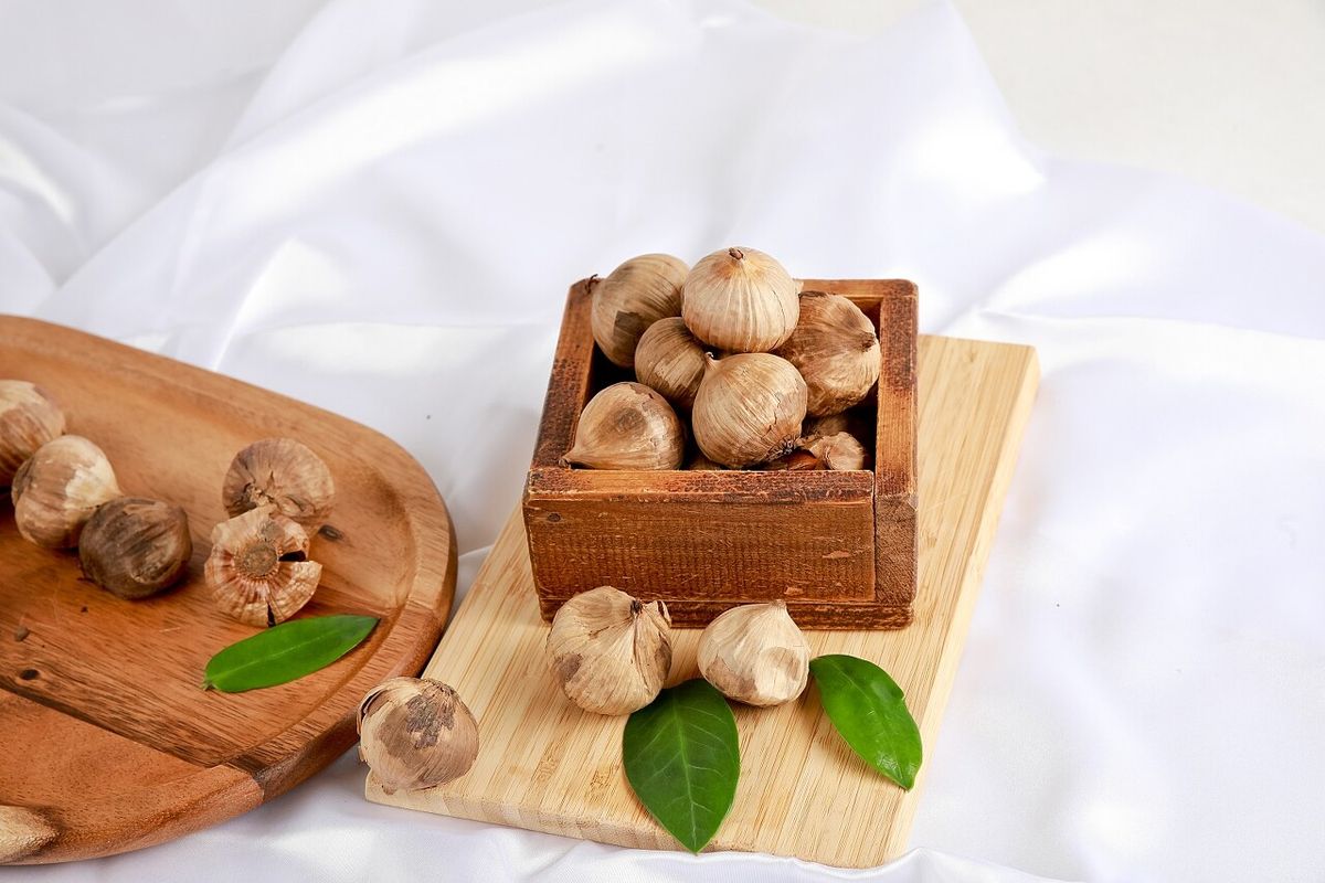 손으로 흑마늘 껍질 벗기는 액션 컷 — 새까만 속 노출, 배경에 산달래 병